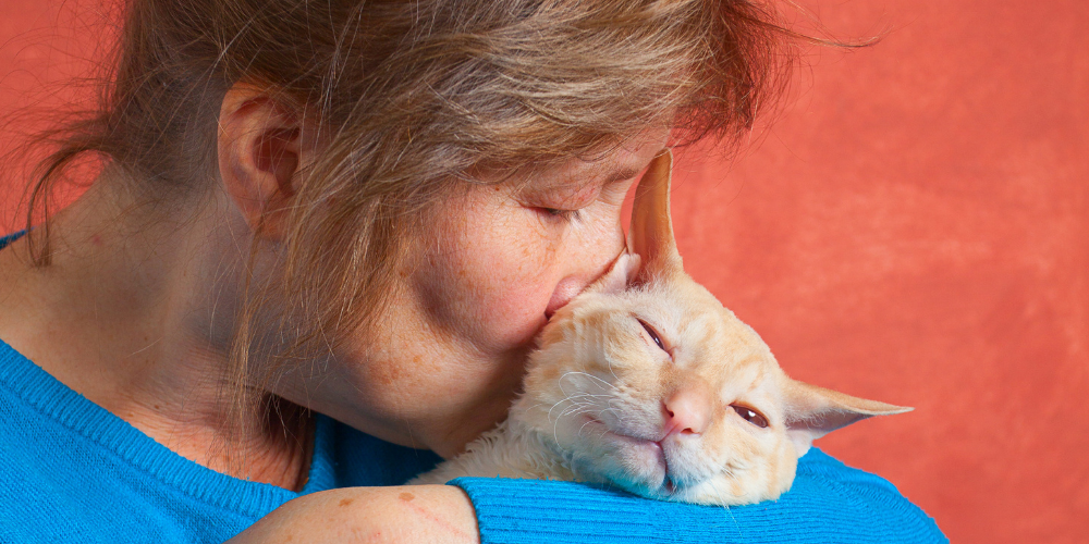 woman cuddling and kissing her cat in her arms