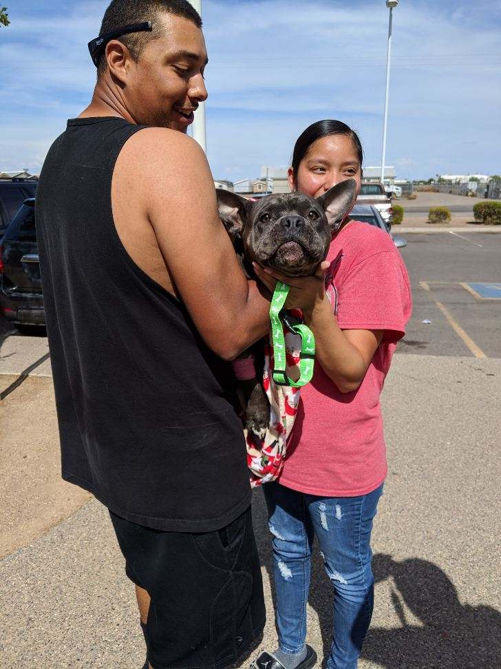 man and woman holding their dog in their arms smiling