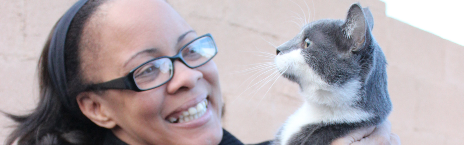 black woman holding up and smiling at her grey and white cat