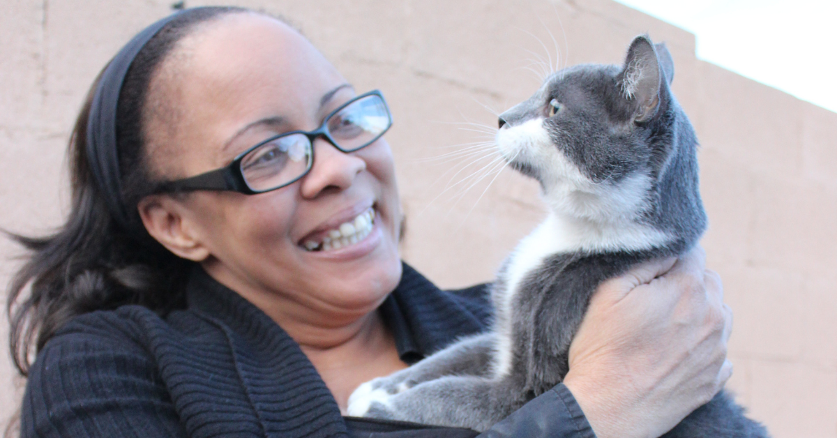 black woman holding up and smiling at her grey and white cat