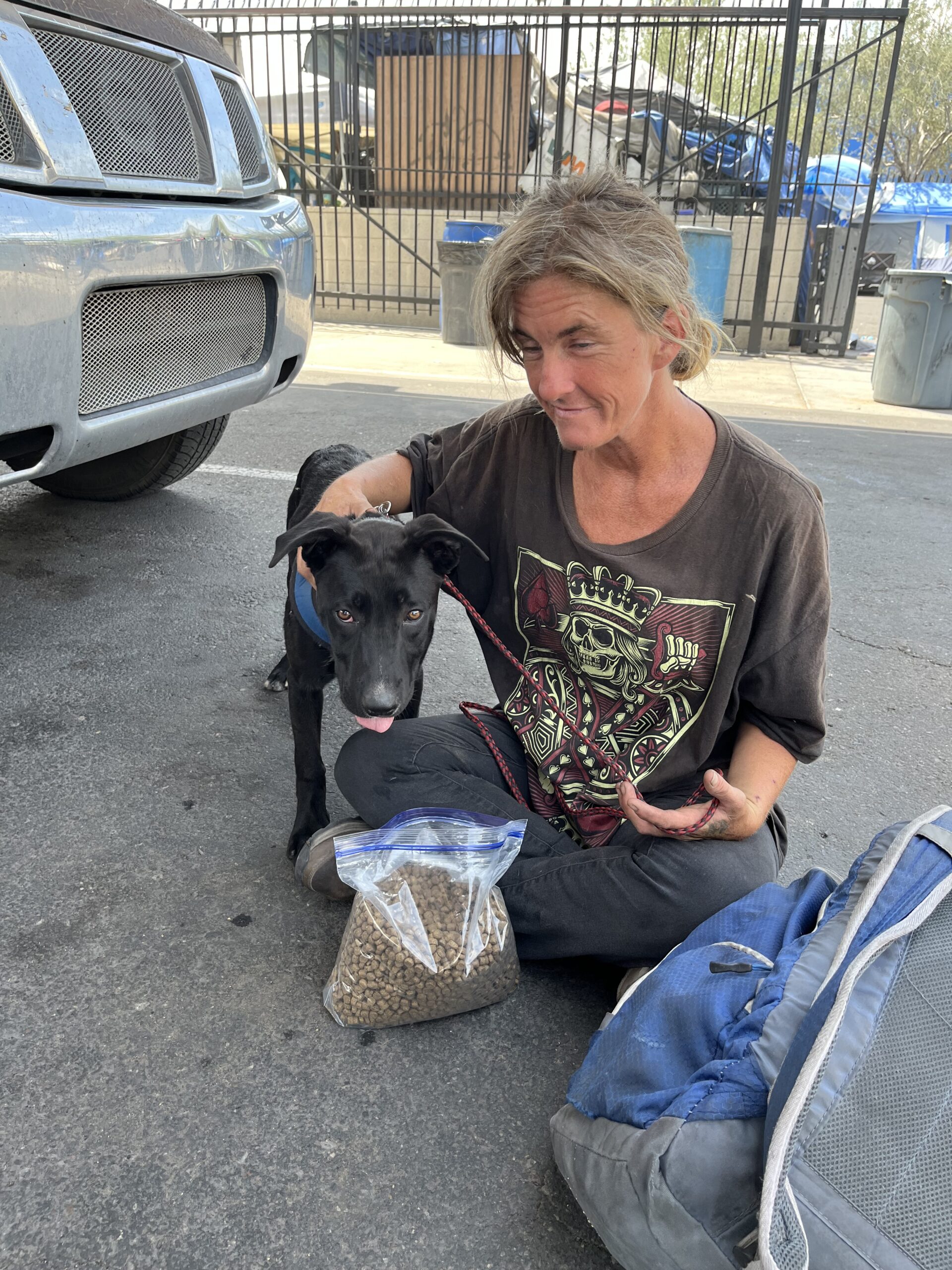 woman sitting with her dog on the ground next to bag of dog food