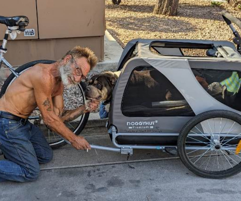 unhoused pet family with a man kneeling down posing for a photo with his dog in a bike dog carrier